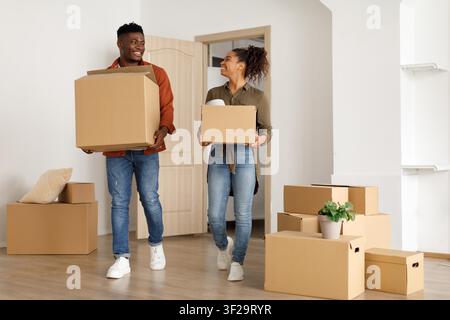 Couple Moving Into New Home Carrying Boxes, Happy African American Pair, Home Lifestyle Stock Photo