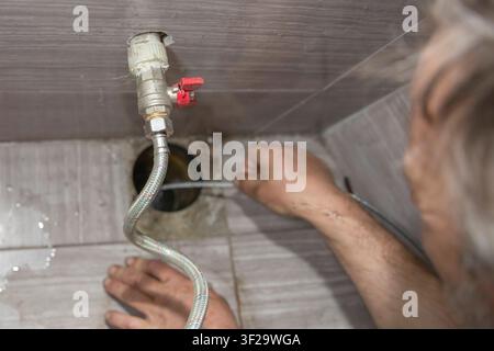 Plumber using drain cleaning cable to clear blocked floor drain indoors Stock Photo