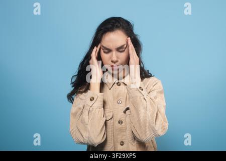 Young Woman Holding Head And Closing Eyes, Feeling Stress Or Pain, Blue Background, Wellness Concept Stock Photo