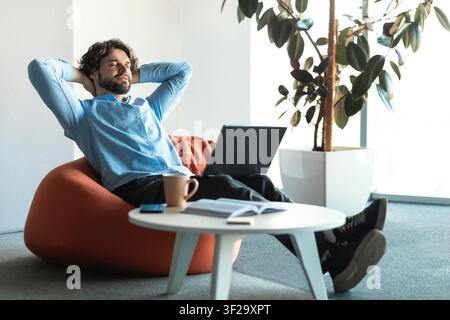 Man Relaxing In Office, Sitting On Bean Bag With Laptop, Happy Mood, Healthcare Concept Stock Photo
