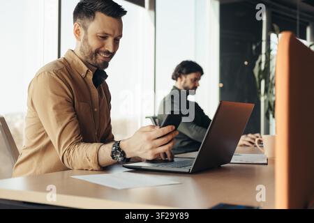 Smiling Caucasian Man Using Smartphone At Office, Business Concept Stock Photo