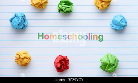 A lined notebook page featuring the word Homeschooling printed in colorful letters, surrounded by paper crumpled balls. Close up. Stock Photo