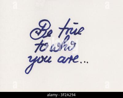 Cursive handwriting in blue ink on white paper spells "Be true to who you are..." The script has an elegant, flowing style. Stock Photo