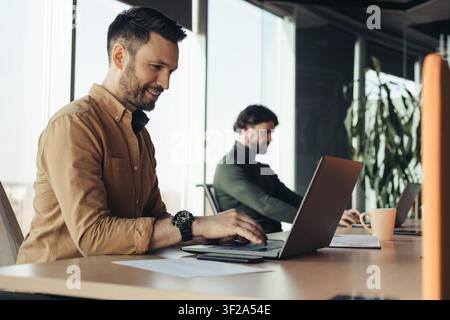 Two Men Working On Laptops In Modern Office, Focused Expression, Business Concept Stock Photo