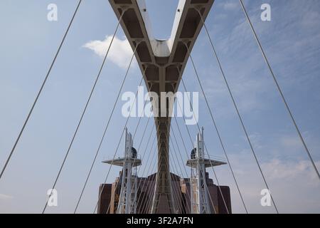 An abstract low-angle close-up of the geometric white steel structure and suspension cables of the Millennium Bridge with a blue sky, Salford Quays. Stock Photo