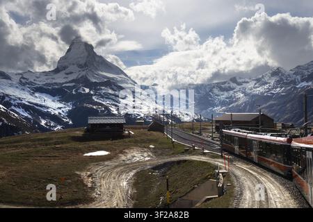View of the Matterhorn mountain towering over the Gornergrat railway train in the alpine landscape with dramatic clouds and snowy peaks in Zermatt, Va Stock Photo