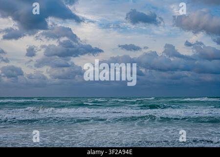 Waves crash on the shore under a cloudy sky at twilight on a beach. Stock Photo