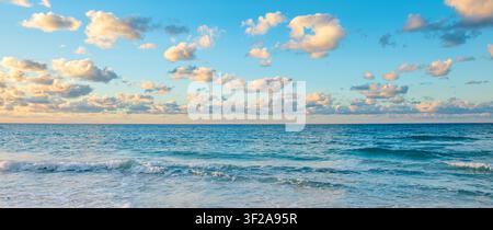 Sunset at the beach with calm waves and fluffy clouds in the sky. Stock Photo