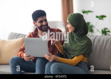 Happy Young Man And Woman Sharing Ideas On Laptop At Home, Relaxing Together Stock Photo