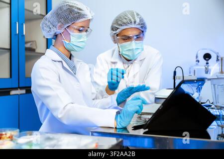 Asian scientists team discussion and checking pharmaceutical research data on digital tablet inside modern science laboratory concept of scientific ph Stock Photo