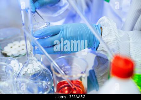 Close up of scientist hand in blue glove using tweezers testing drug tablet sample inside pharmaceutical research laboratory. concept of formulation t Stock Photo