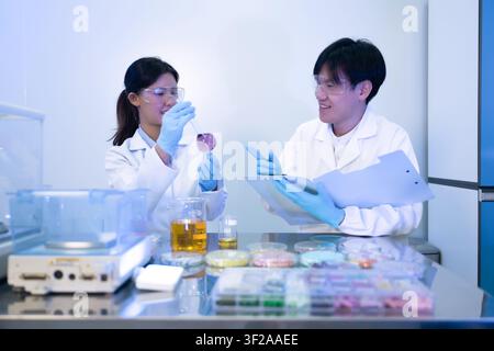 Asian two scientists enjoy collaborating chemical experiment laboratory research team, Researchers analyzing liquid sample laboratory glassware, Takin Stock Photo