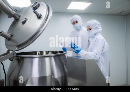 Two pharmaceutical factory workers in cleanroom suits checking production. Business and science concept in pharmaceutical industry. cleanroom manufact Stock Photo