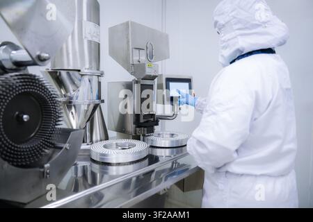 Pharmaceutical worker using medicine control digital panel in factory. Operating capsule filling machine via touchscreen in clean room. Pharmaceutical Stock Photo