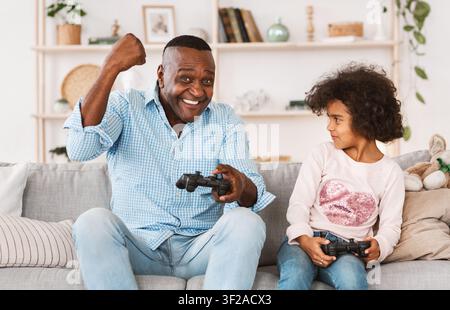 Having fun during lockdown. African American kid playing video games with granddad at home Stock Photo