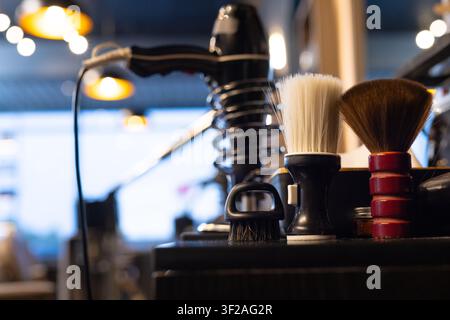 Shaving brush white bristles, palm brush black bristles, red handle brush sitting on dark counter Stock Photo