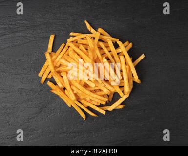 Fried chips sticks on black plate, finger potato chips, golden shoestring fries pile, French fries, roasted potatoes, frites on dark stone table backg Stock Photo