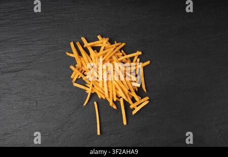 Fried chips sticks on black plate, finger potato chips, golden shoestring fries pile, French fries, roasted potatoes, frites on dark stone table backg Stock Photo