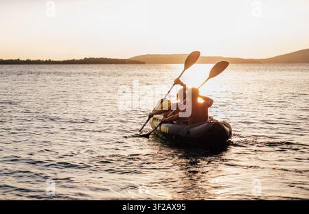 Two people rowing inflatable kayak on Adriatic Sea at sunset near Sibenik Croatia, couple paddling during golden evening light, active summer vacation Stock Photo