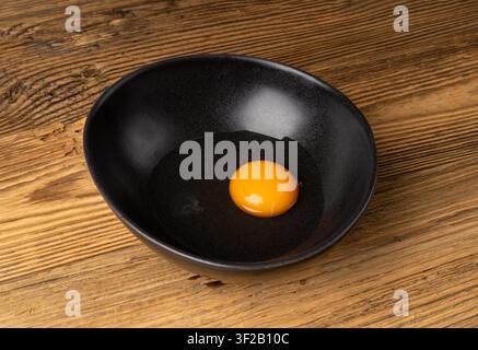 One Broken Egg in Black Bowl, Raw Yolk and White, Fresh Broken Organic Chicken Egg on Wooden Rustic Background Stock Photo