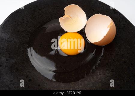 One Broken Egg in Black Bowl, Raw Yolk and White, Fresh Broken Organic Chicken Egg on Wooden Rustic Background Stock Photo