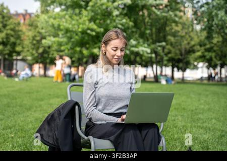Calm focused middle aged woman in city park using laptop. Distance working, digital nomad mobility Stock Photo