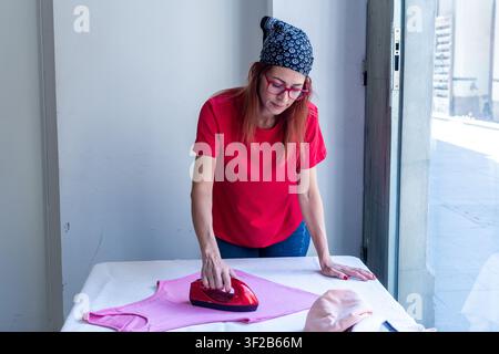 Woman ironing clothes on a pressing table in a bright room Stock Photo