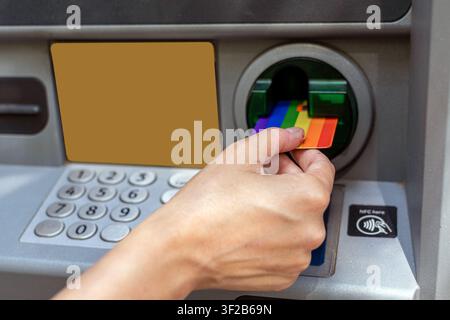Hand inserting rainbow credit card into atm machine Stock Photo