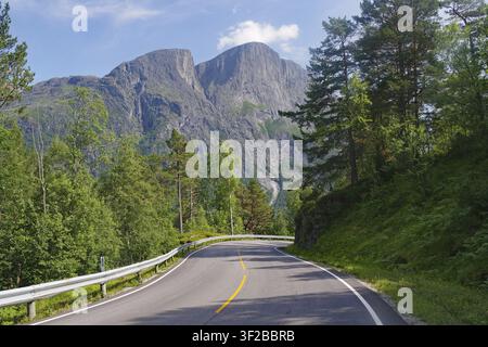 A winding road leads through thick forests with large mountains in the background, Eikesdalen. Aursjoevegen, More og Romsdal, Norway Stock Photo