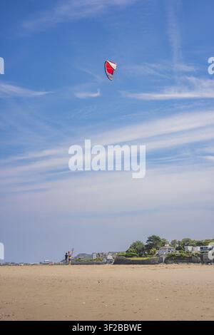 A red kite flies over a beach with people and bright skies, low tide, Howth beach, Ireland Stock Photo