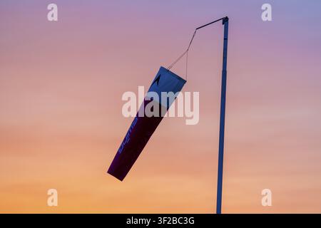 A windsock shows the wind direction during a dramatic sunset in an orange sky Stock Photo