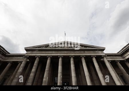 The neoclassical Greek Revival facade of the British Museum, with Ionic columns, sculpted pediment and Union flag, Bloomsbury, London, England, UK Stock Photo