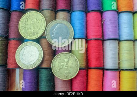 Flat lay view of Euro coins placed on top of neatly arranged rows of colorful sewing thread spools symbolizing inflation, economic crisis, and rising Stock Photo