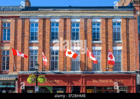 Historic brick commercial building displaying Canadian flags. A business sign reading "au-then-ti-ci-ty" Stock Photo