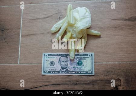 Overhead view of crumpled protective latex gloves resting on a US five dollar banknote on a wooden surface, representing healthcare fraud, medical cor Stock Photo