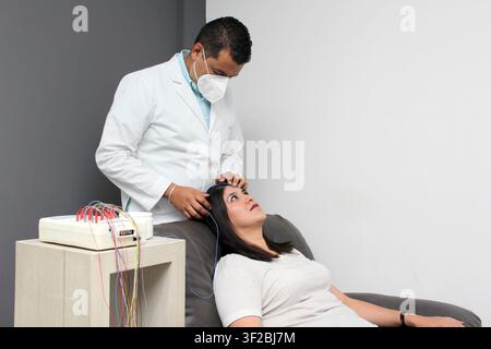 Latin neurologist medical specialist doctor measures the head of his Latin woman patient to stick the electrodes and check the brain activity Stock Photo