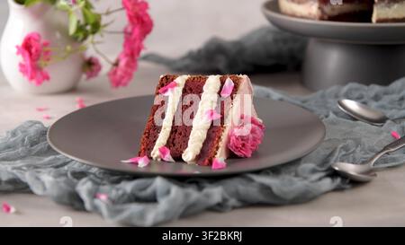 An eye level studio shot captures a slice of layered velvet cake with white cream filling and pink rose petal accents. Bright soft lighting highlights Stock Photo