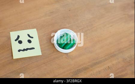 Pain sticky note placed beside green medicine capsules on wooden background, suitable for anxiety, treatment, therapy, medication Stock Photo