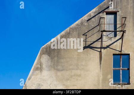 Weathered facade of an old building featuring an elevated wooden door with a small metal platform and blue sky. Brandmauer, Firewall, Architecture. Stock Photo