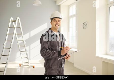 Smiling construction worker with hard hat and clipboard in bright interior Stock Photo