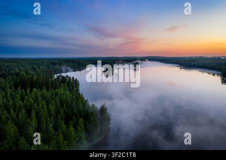 Aerial view of Laaminki lake surrounded by dense coniferous forests with morning mist rising from the water during sunrise in Kangasniemi, Etela-Savo, Stock Photo