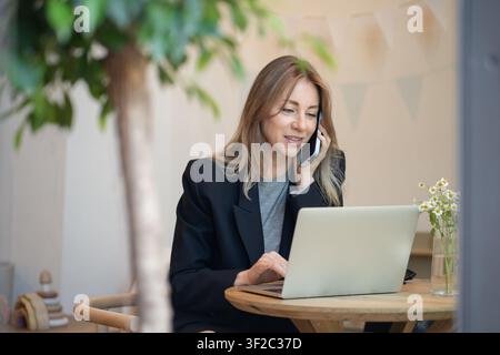 Busy businesswoman with laptop talking on smartphone in coffeeshop coffeehouse with business project Stock Photo