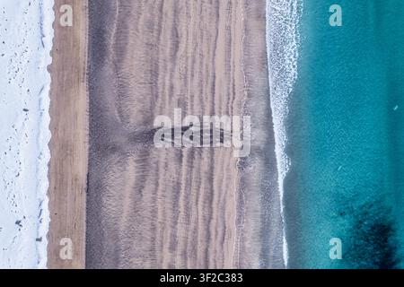 Aerial view of the coastline of Senja with snow-covered sand, dark patterns in the wet sand, and turquoise sea water in Senja, Troms, Norway. Stock Photo