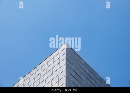 Minimalist architectural photograph of a modern glass building corner forming a geometric triangular composition against a clear blue sky. Stock Photo