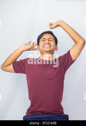 Young Indonesian male model holding the back of his hair with both hands posing against white studio background. Stock Photo