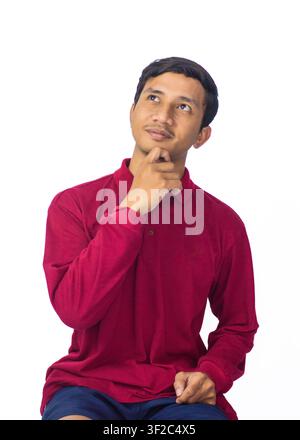 Handsome Asian male model in red ethnic shirt standing with folded hands for Eid Mubarak greeting on white background. Stock Photo