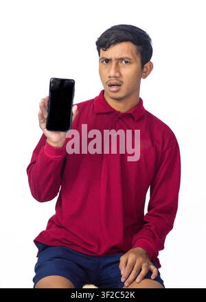 Young Asian man wearing red traditional shirt holding smartphone with blank screen showing mockup isolated on white background. Stock Photo