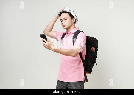 Asian man backpacker hold mobile phone with confused expression. travelling concept. on isolated background Stock Photo