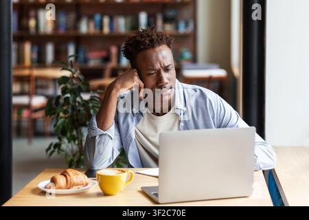 Online education. Focused black guy studying for difficult exam on laptop at coffee shop Stock Photo