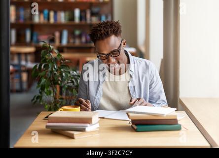 Happy black guy studying or working with books at coffee shop Stock Photo